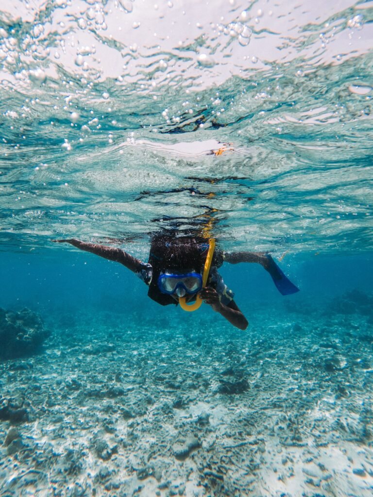 Snorkeler swimming underwater with blue fins and a mask over a sandy reef bed near the Phi Phi Islands, Thailand.