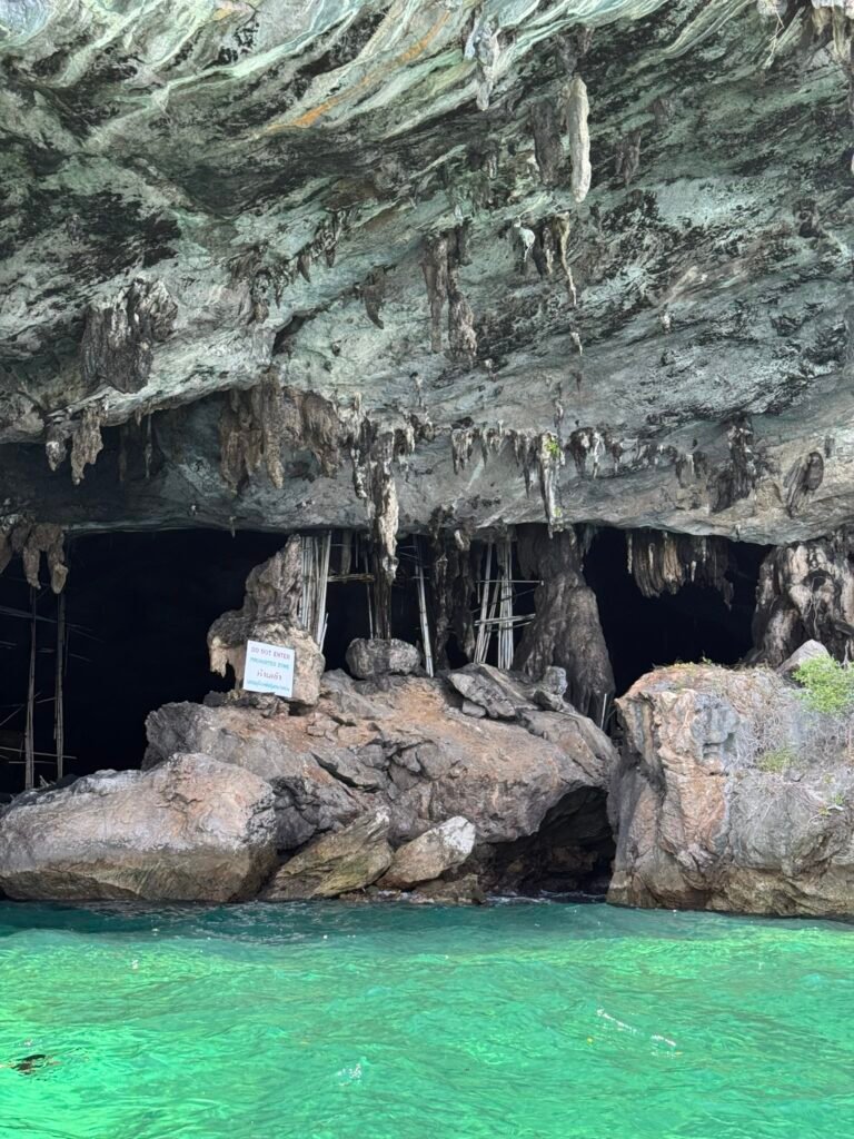 Viking Cave on Phi Phi Leh viewed from the water, showing stalactites hanging from the cave ceiling, bamboo scaffolding inside, and a "Do Not Enter" sign at the entrance.